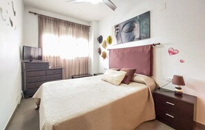 A bedroom with a bed, a TV, a dresser, and a painting on the wall.