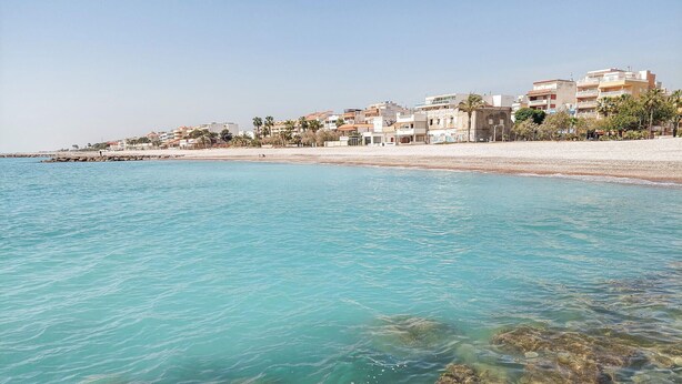 Eine Küstenstadt mit Gebäuden entlang des Strandes, klarem türkisblauem Wasser und Felsformationen.