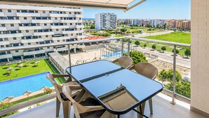 Ein Balkon mit Glastisch und Stühlen mit Blick auf einen Pool und eine angelegte Grünfläche.
