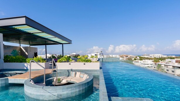 A rooftop infinity pool with a seating area, a hot tub, and a covered patio.
