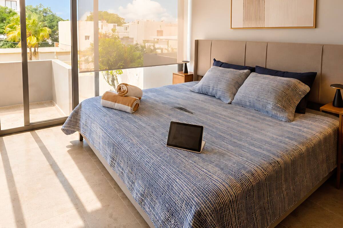 Un dormitorio con cama, ventilador de techo, mesita de noche, ventana y vistas al exterior.