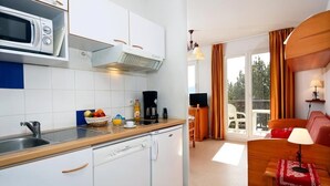 Cocina compacta con microondas, lavamanos y un refrigerador pequeño. Cuenta con un comedor con mesa y sillas, además de una sala de estar con sofá y lámpara.