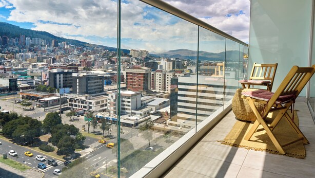 Ein Balkon mit Blick auf die Stadt, ein Korbstuhl und ein kleiner Teppich.