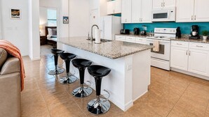 Una cocina moderna con armarios blancos, encimera de granito y una isla central con taburetes de bar.