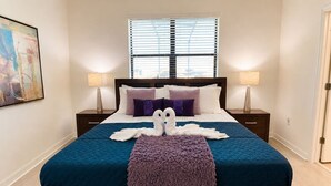 Una cama con colcha azul, dos almohadas moradas y una manta morada.