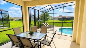 Un patio cubierto con una mesa y sillas, una piscina y vistas a una zona residencial.