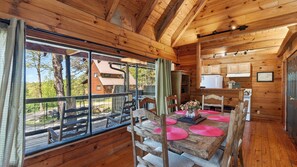 A wooden cabin interior with a dining area, kitchen, and large windows overlooking a forest. - Elijah's, Isaiah's, Jack's, Sónyah's & Anna's Cabins by Avantstay Sleeps 30 5 Cabins + Hot Tubs Townsend + Smokies Access (Townsend)