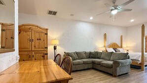 A room with a wooden dining table, a sofa, a bed, and a ceiling fan. - Amira Resort #17 | Studio | Near Pool & Pickleball (Saint George)