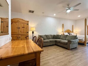 A room with a wooden dining table, a sofa, a bed, and a ceiling fan. - Amira Resort #17 | Studio | Near Pool & Pickleball (Saint George)