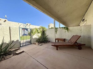 A covered patio area with a wooden lounge chair, a small table, and a gate leading to a street. - Amira Resort #17 | Studio | Near Pool & Pickleball (Saint George)