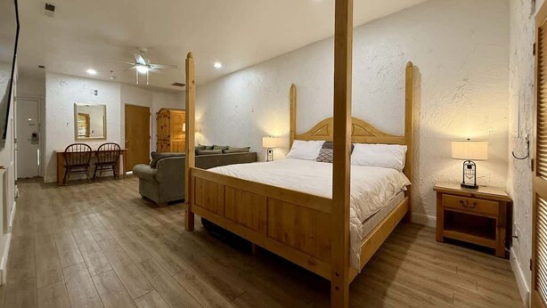 A four-poster bed with a wooden frame, a sofa, a dining table with chairs, and a bedside table with a lamp. - Amira Resort #17 | Studio | Near Pool & Pickleball (Saint George)
