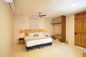 Une chambre à coucher comprenant un lit, un ventilateur de plafond, un climatiseur fixé au mur, une porte en bois et un petit meuble en bois.