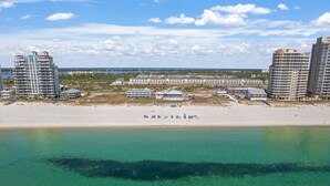 Un hotel frente a la playa con varios edificios altos, una playa de arena y una vista despejada del océano.
