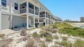 Hotel frente a la playa con varios balcones, una playa arenosa y un cielo azul despejado.