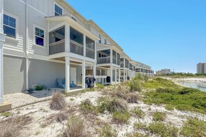 Ein Strandhotel mit mehreren Balkonen, ein sandiger Strand davor und ein klarer, blauer Himmel.