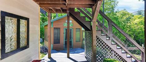 A wooden structure with a staircase leading to a door, a bench, and a view of greenery.