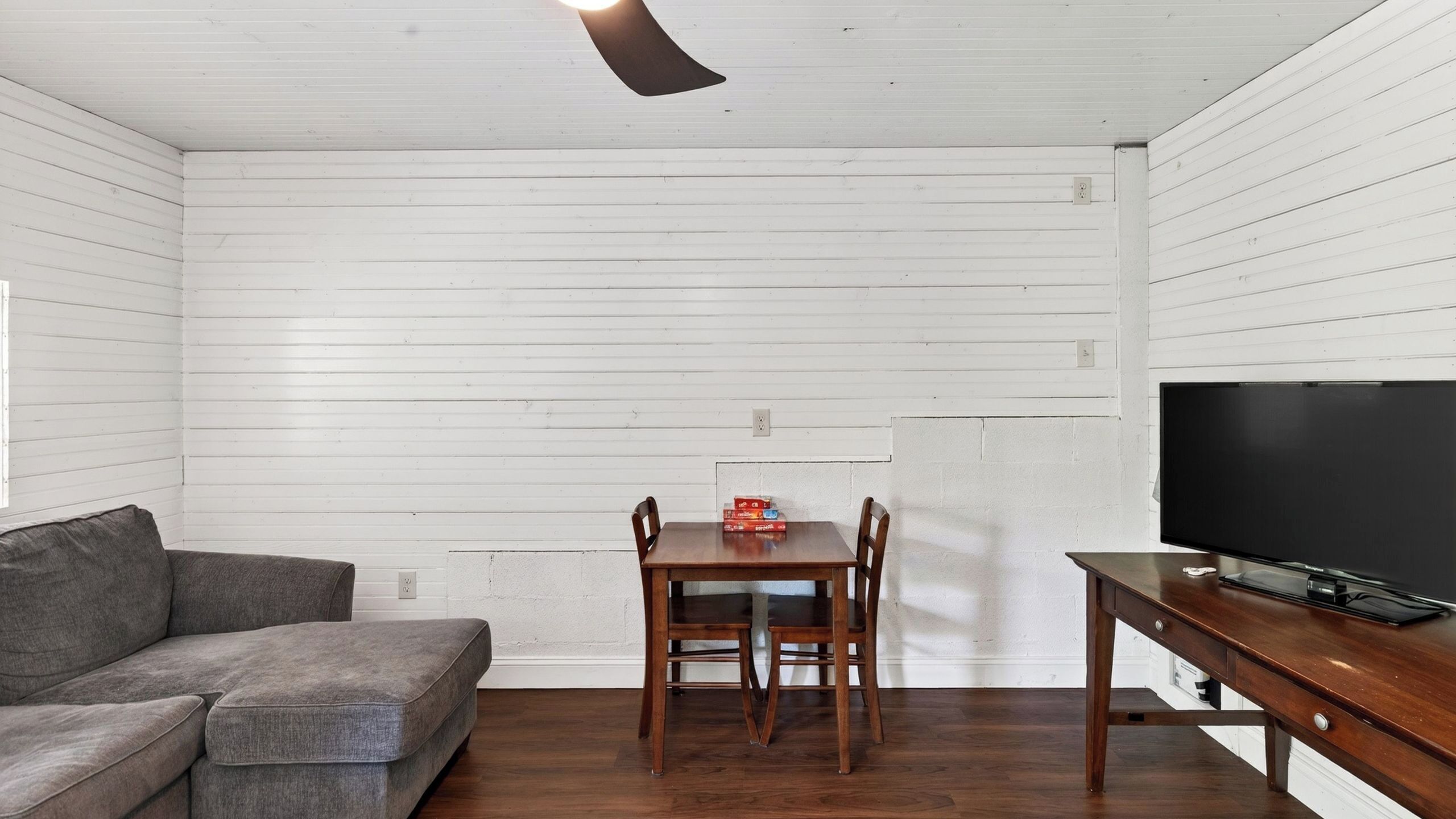 A room with a wooden table, two chairs, a sofa, and a flat-screen TV.