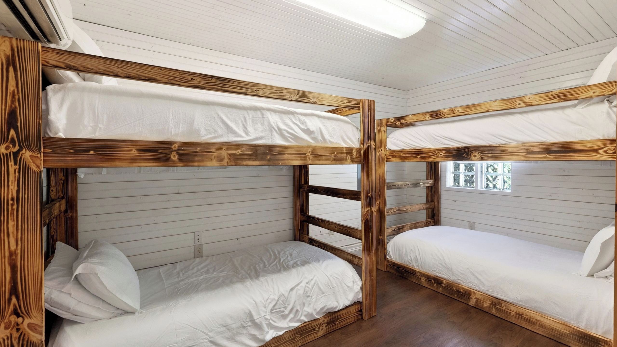 A bunk bed room with white bedding, wooden frames, and a window with a view.