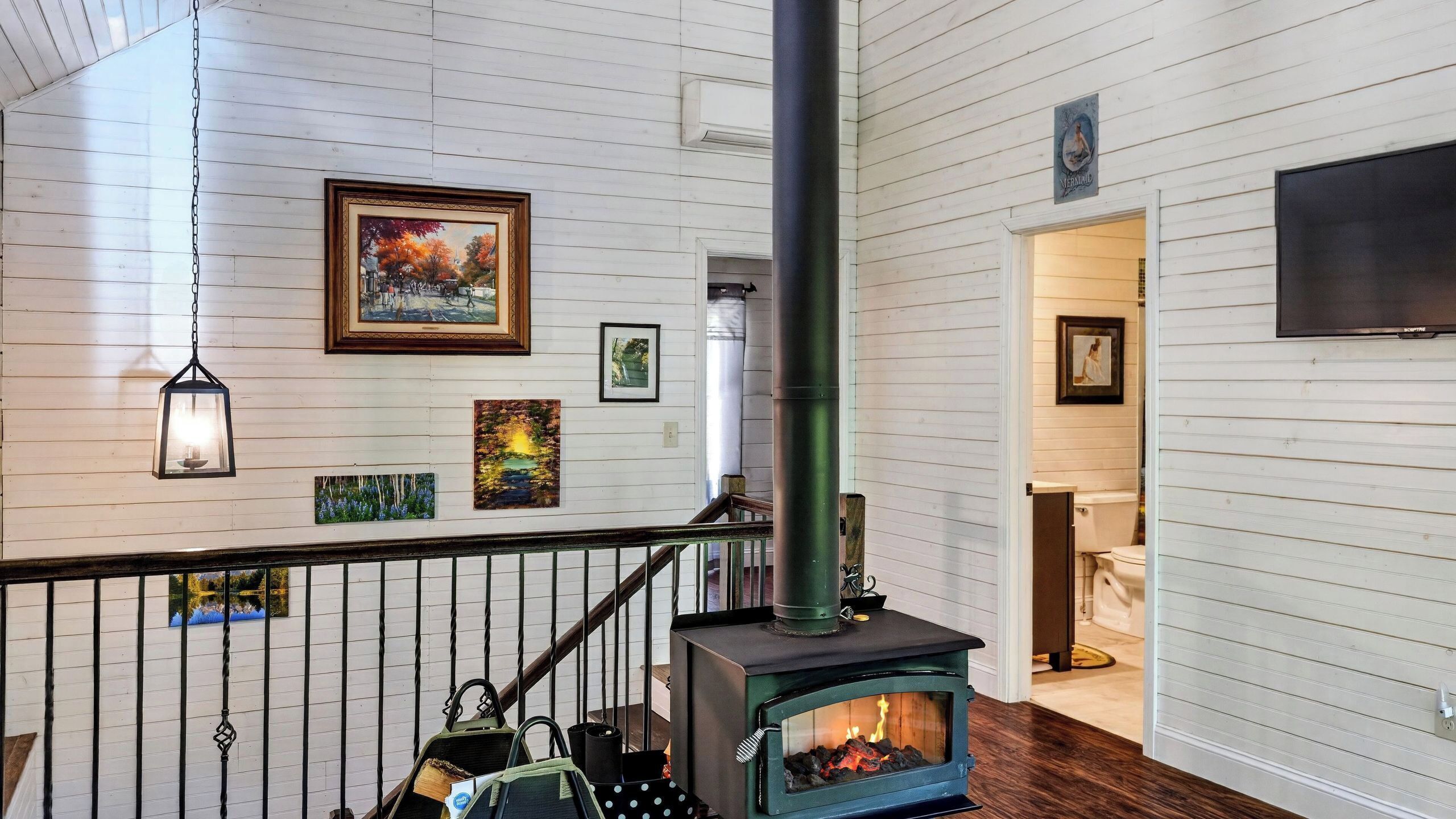 A room with a wood-burning stove, a staircase, and a hanging lantern.