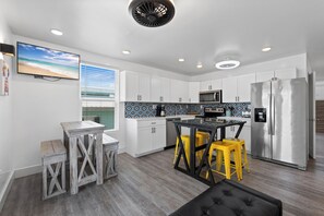 A modern kitchen with white cabinets, a stainless steel refrigerator, and a dining area with a black table and yellow stools. - Full Home Duplex, Includes BOTH Sides w/ Private Pool Steps from Beach (Gulf Shores)