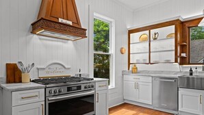 A kitchen with white cabinetry, a stainless steel range, and a wooden hood. - The Anna Bell Suite at historic Jeter Farmhouse (Gladewater)