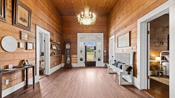 A wooden interior with a chandelier, framed pictures, a grandfather clock, and a bench. - The Anna Bell Suite at historic Jeter Farmhouse (Gladewater)