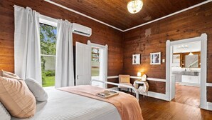 A bedroom with a bed, a desk, and a chair, a bathroom with a sink, and a view of the outdoors. - The Anna Bell Suite at historic Jeter Farmhouse (Gladewater)