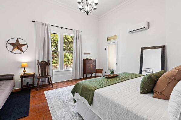 A bedroom with a bed, a chair, a dresser, a lamp, and a window with curtains.