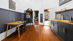 A narrow hallway with a wooden table and chairs, a coffee bar, and a kitchen area with cabinets and a countertop. - The Leonidas Suite at historic Jeter Farmhouse (Gladewater)