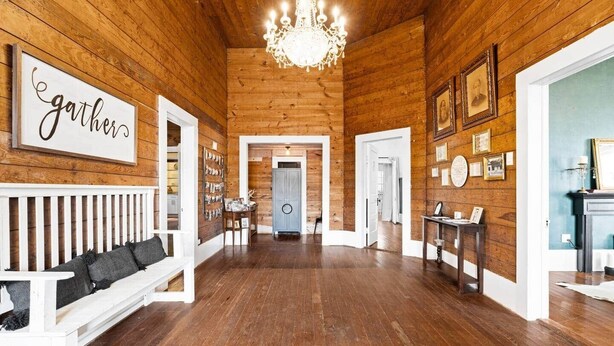 A wooden interior with a chandelier, a bench, a wall with a 'gathers' sign, and a hallway leading to another room. - The Leonidas Suite at historic Jeter Farmhouse (Gladewater)