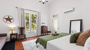 A bedroom with a bed, a chair, a dresser, a lamp, and a window with curtains. - The Leonidas Suite at historic Jeter Farmhouse (Gladewater)