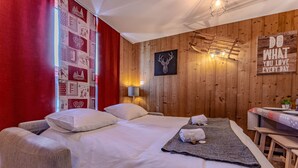 Quarto de hotel com parede de madeira, cama com roupa de cama branca, cortina vermelha, arte na parede com a imagem de um veado e um letreiro com frase motivacional.