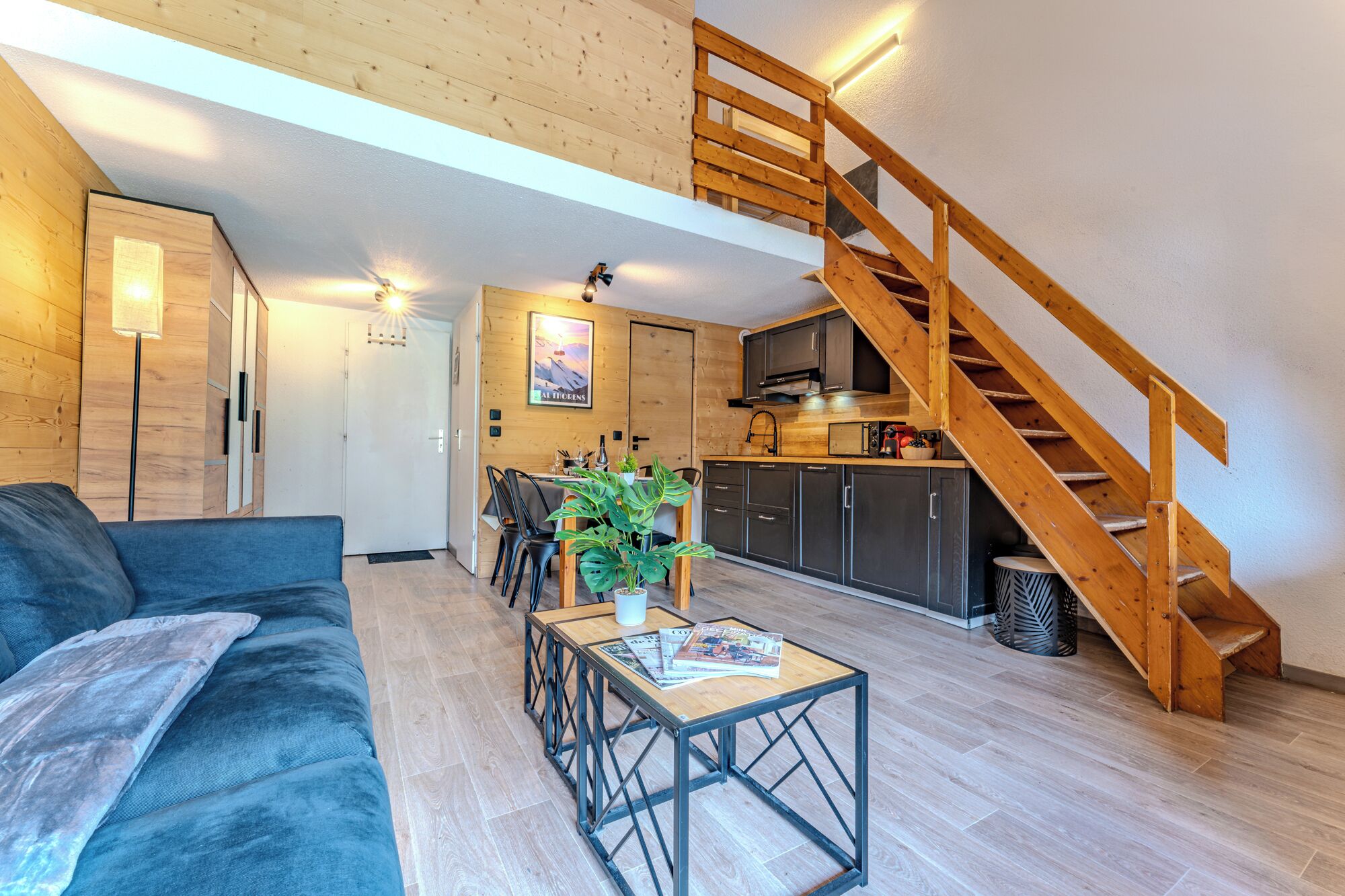 A modern living room with a wooden staircase, a dining area, and a kitchen.