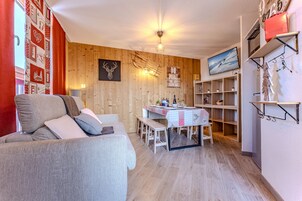 En hyggelig stue med sofa, spisebord med stole, trævæg og et ophængt fjernsyn.