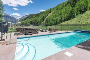 Une piscine avec vue sur les montagnes et un espace clos aménagé avec des sièges extérieurs.
