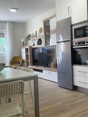 A modern kitchen with a refrigerator, oven, microwave, and a flat-screen TV. - A casa da tía María, Razo, Costa da Morte (Nétoma)