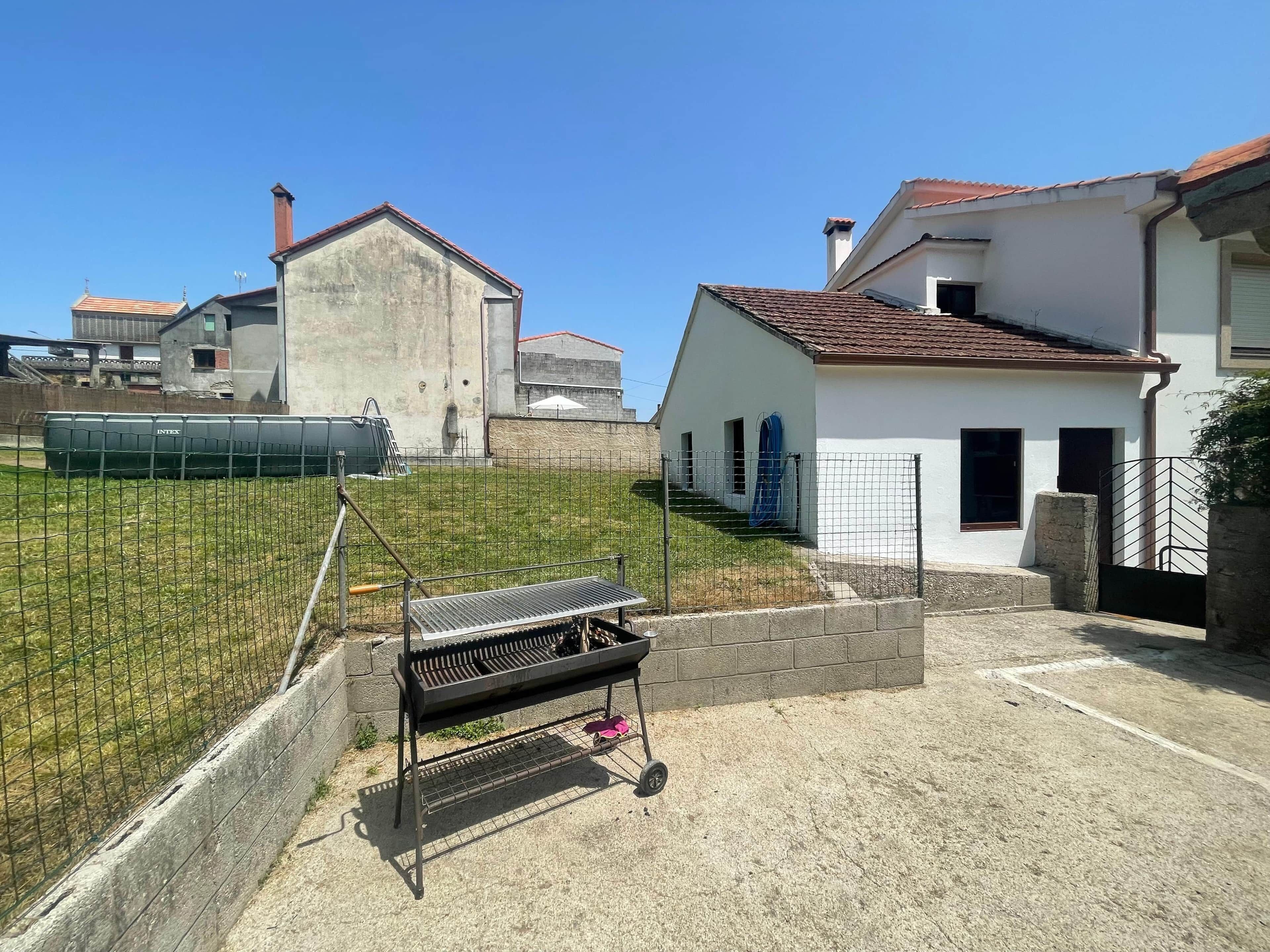 Un barrio residencial con una reja metálica, un patio cercado y una casa blanca de techo rojo.