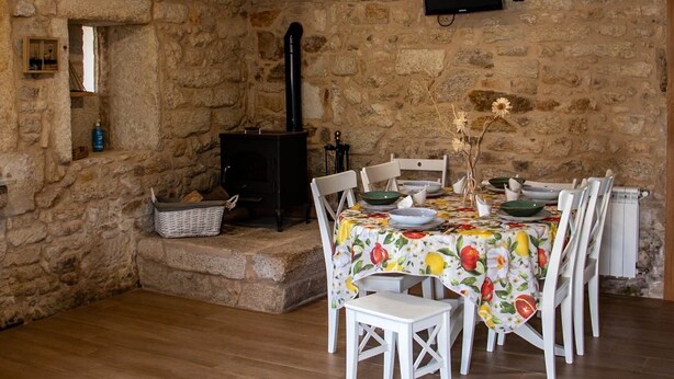 Una habitació rústica amb parets de pedra, una llar de foc, una taula de dinar amb cadires i un televisor fixat a la paret.