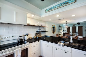 A kitchen with white cabinetry, a black countertop, and a stove. There is a shelf with dishes and a clock on the wall.