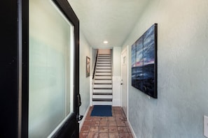 A hallway with a staircase, a blue mat, and a painting on the wall.