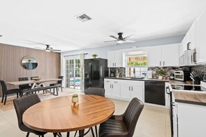 Eine moderne Küche mit weißen Schränken, einem schwarzen Kühlschrank und einer Essecke mit Holztisch und Stühlen.