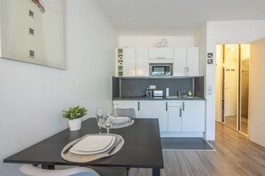 Cocina moderna con armarios blancos, un microondas y un lavamanos. Hay una mesa de comedor con platos y vasos.