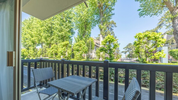 A balcony with two chairs and a table, overlooking a street with trees and buildings. - Studio des Ouvres - Welkeys (Deauville)