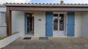 Un bâtiment avec un toit recouvert de tuiles, une porte avec des volets bleus et un petit porche.