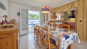 Un coin repas avec une table dressée pour quatre personnes, des chaises en bois, un luminaire suspendu et une vue à travers une porte vitrée.