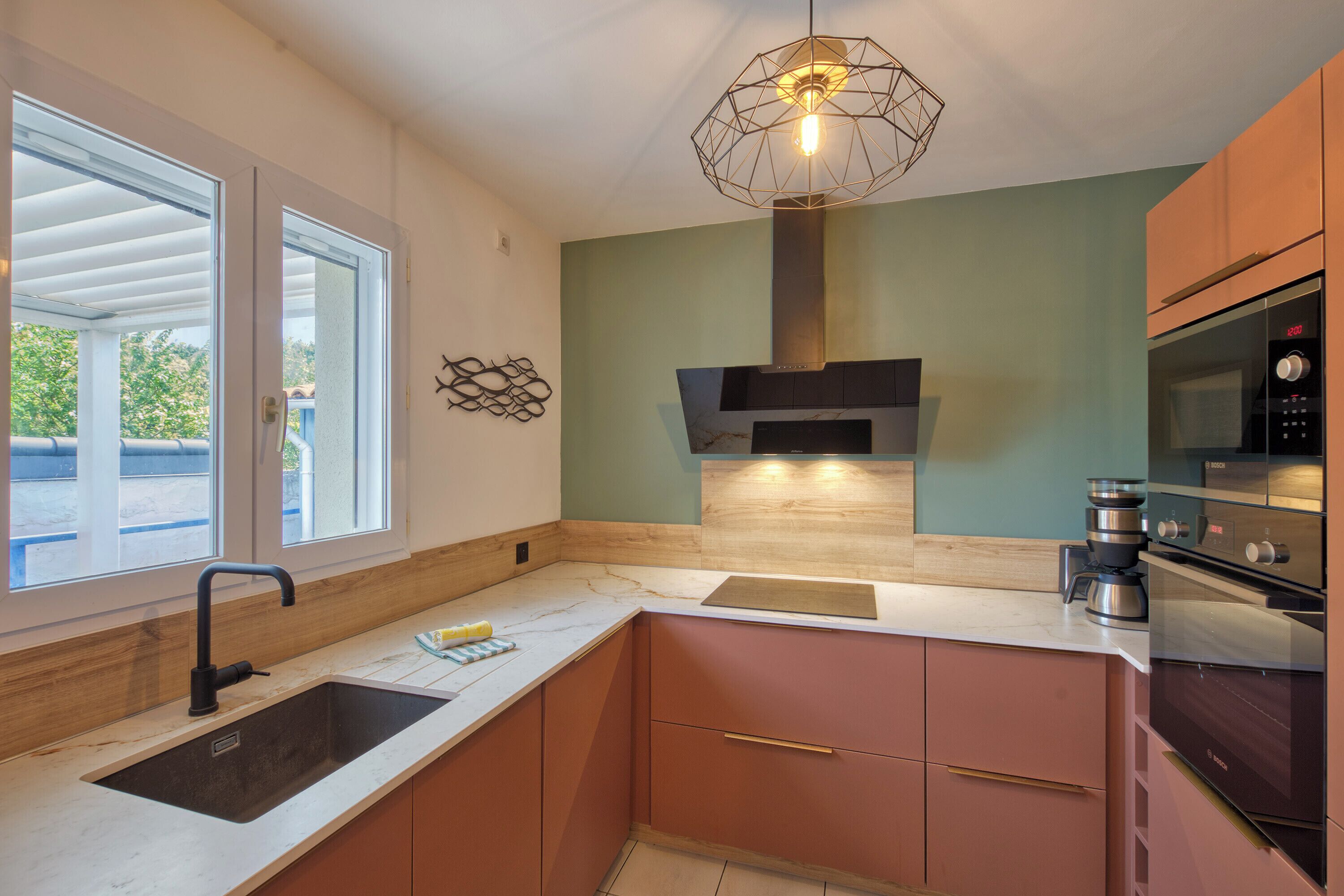 Een moderne keuken met een ingebouwde oven, een koffiezetapparaat van roestvrij staal, en een raam dat natuurlijk licht binnenlaat.