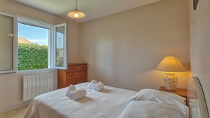 Une chambre à coucher avec un lit, une commode, une lampe et une fenêtre donnant sur un paysage verdoyant.