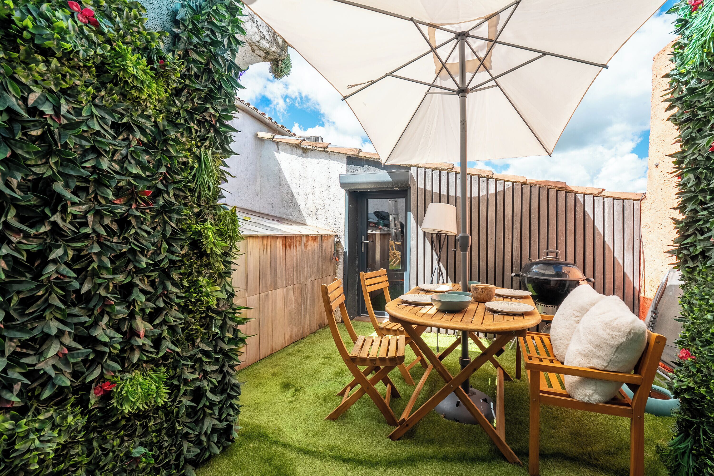 A patio with a table and chairs, a grill, and a large umbrella.
