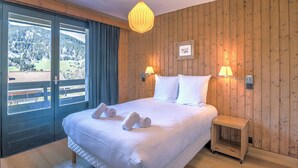 Una camera da letto con un letto grande, pareti in legno, due lampade sui comodini, un piccolo tavolo da notte e vista su un paesaggio montuoso attraverso una porta scorrevole.
