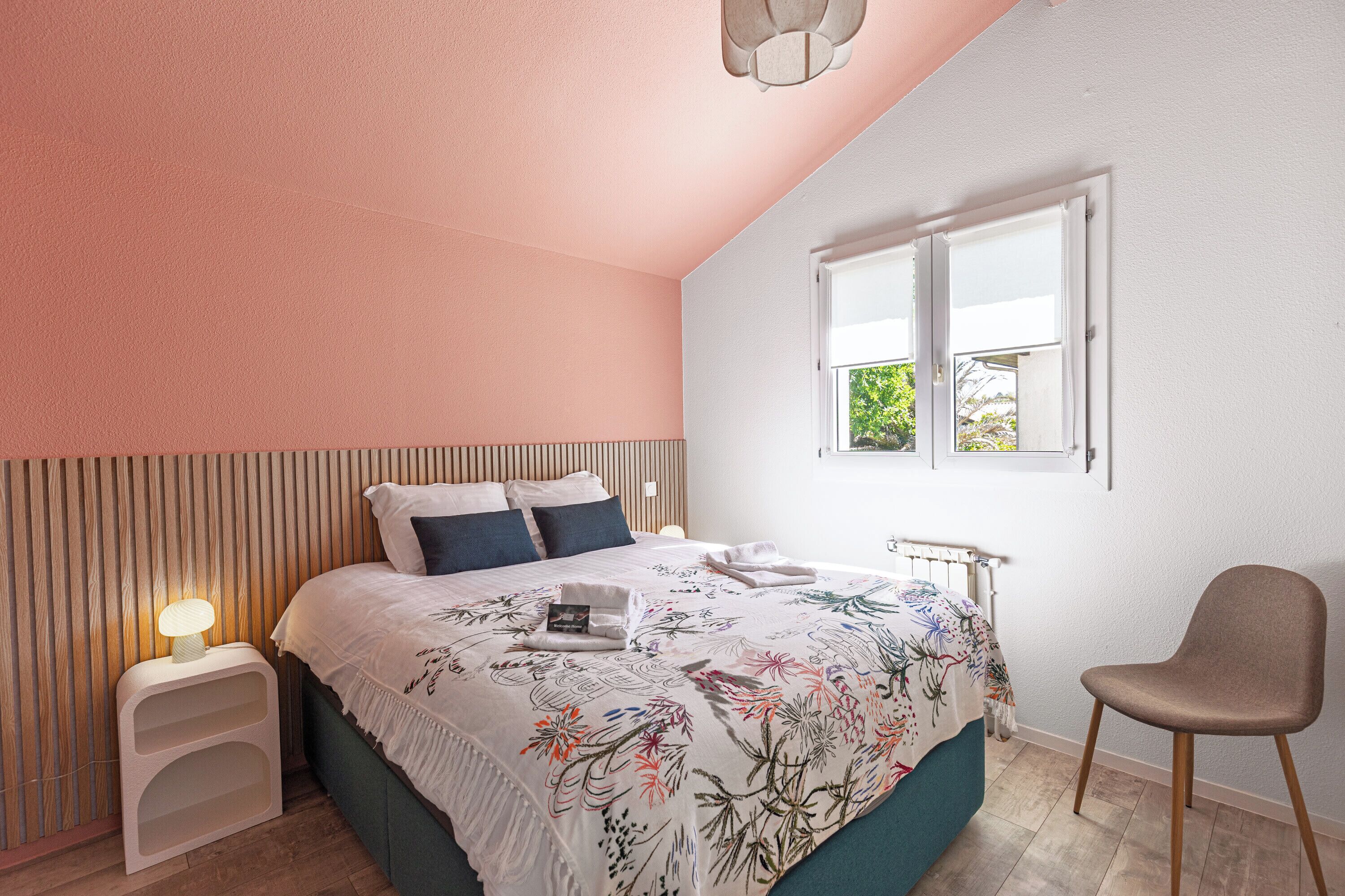 Une chambre à coucher avec un lit, une table de chevet avec une lampe, une chaise, une fenêtre et un radiateur.